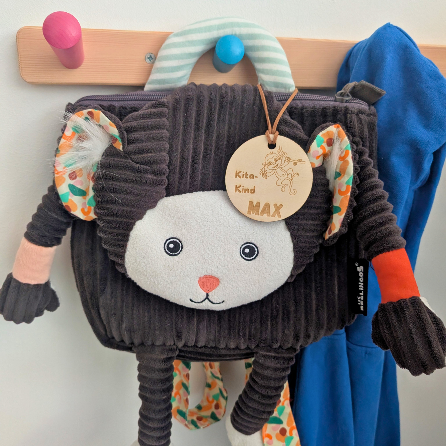 Holzanhänger mit Dino-Motiv hängt am pinken Kinderrucksack vor Kita-Garderobe